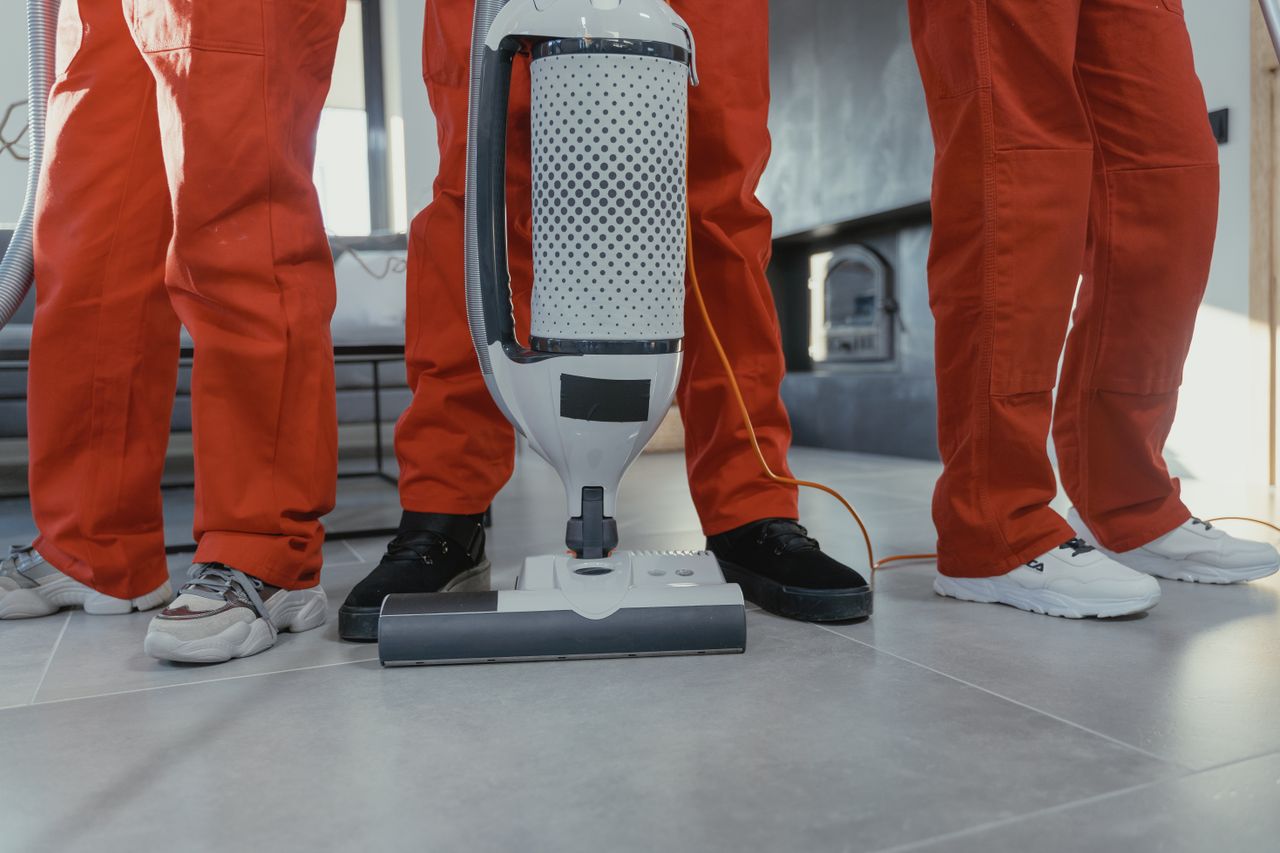 A team of professional cleaners dressed in red uniforms using a vacuum cleaner indoors.